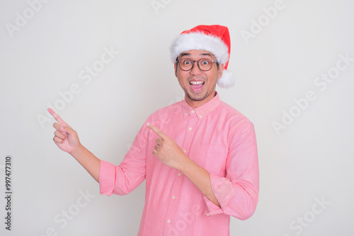 A man wearing santa hat pointing beside him with amazed expression photo