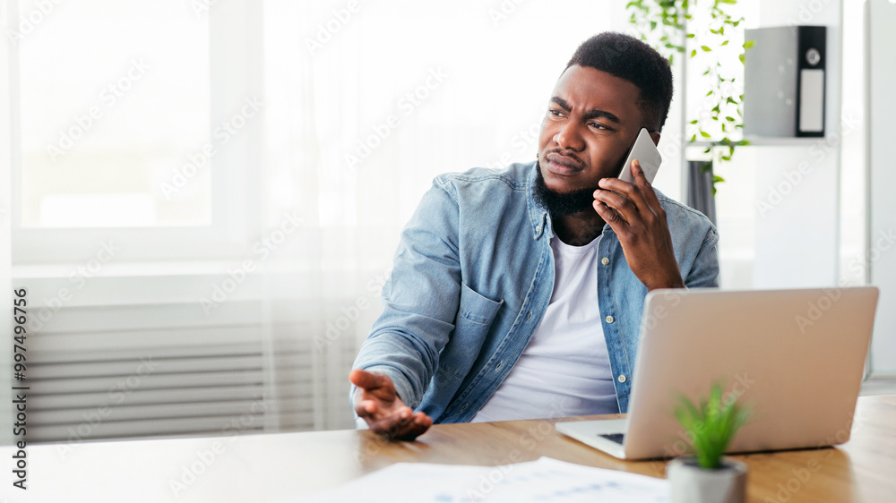 © Prostock-studio - Failure and crisis concept. Upset african american employee getting bad news on phone while sitting at his workplace in office, copy space