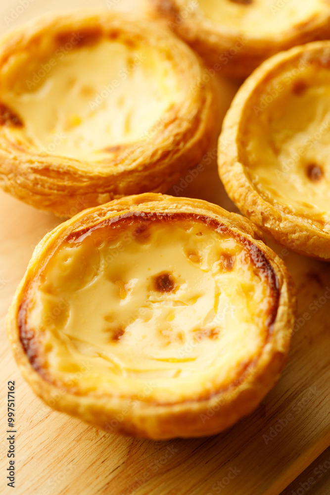 Stack of Portuguese sweet dessert egg tart or Pastel de Nata on wooden board on wooden table. Selective focus. Stack of Portuguese sweet dessert egg tart or Pastel de Nata on wooden board on wooden table. Selective focus.