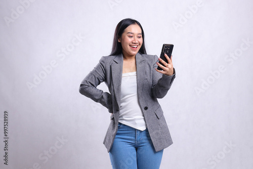 beautiful young office girl asia cheerful to mobile phone hold waist, holding cellphone wearing gray suit isolated on white background. for technology, lifestyle, shopping, transaction content