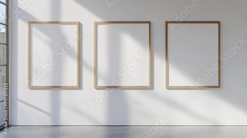 A minimalist interior design featuring three identical rectangular picture frames mounted on a plain white wall.