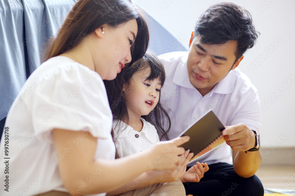 Fototapeta premium Happy Family Sitting On Floor And Reading A Book Together At Home 