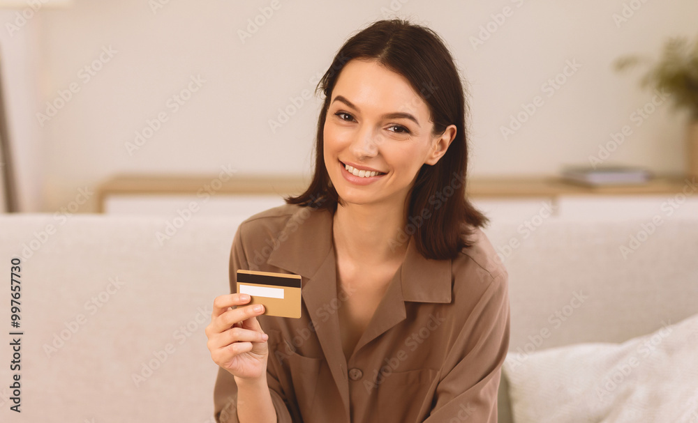 Easy Money Transfer. Happy young woman holding credit card, sitting on couch and looking at camera, copyspace Easy Money Transfer. Happy young woman holding credit card, sitting on couch and looking at camera, copyspace