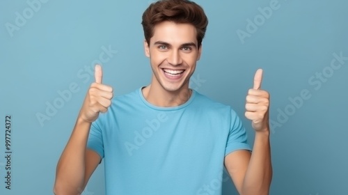 A cheerful man in a blue shirt giving two thumbs up in front of a blue backdrop, exuding positivity and enthusiasm.