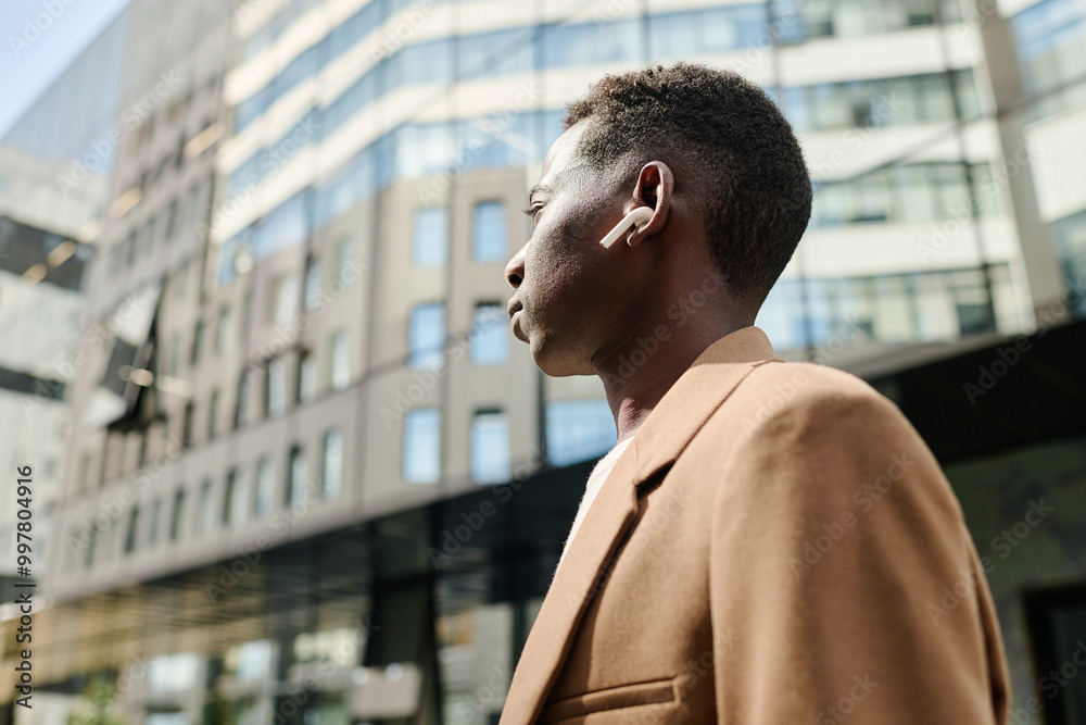 Low angle view medium closeup of young Black man wearing wireless earphones listening to music on way to work Low angle view medium closeup of young Black man wearing wireless earphones listening to music on way to work