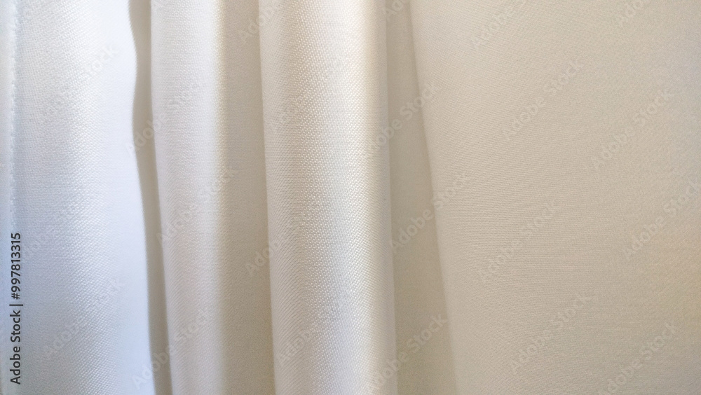 Background material with light shining into the white curtain. white pleat fabric background. All white curtains have a soft, smooth backing Background material with light shining into the white curtain. white pleat fabric background. All white curtains have a soft, smooth backing