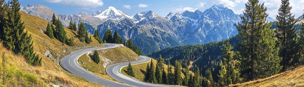 Fototapeta premium A winding mountain road with sharp curves, lined with tall pine trees and snowcapped peaks in the distance