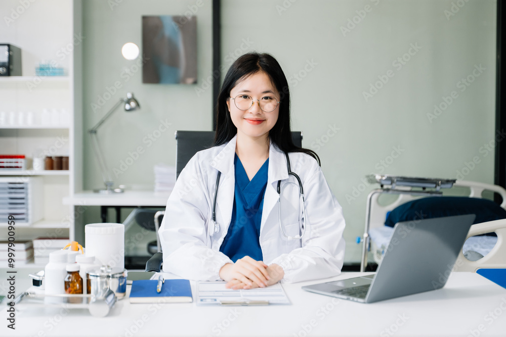 Confident young female doctor in white medical uniform sit at desk working on computer. Smiling use laptop write in medical journal Confident young female doctor in white medical uniform sit at desk working on computer. Smiling use laptop write in medical journal