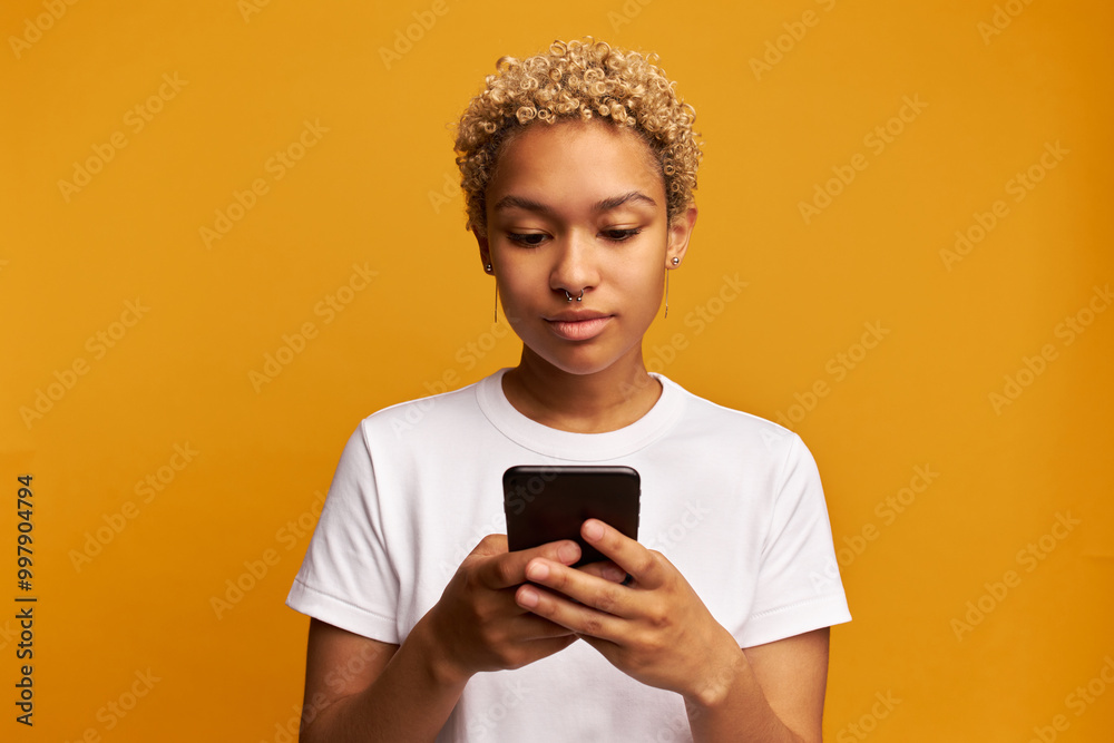 Portrait of calm concentrated female smm specialist or copywriter working online on smartphone, making corrections in article before posting and sharing in social media, isolated on yellow background Portrait of calm concentrated female smm specialist or copywriter working online on smartphone, making corrections in article before posting and sharing in social media, isolated on yellow background