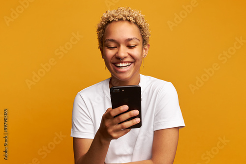 Portrait of laughing black cheerful girl holding smartphone and laughing out loud while browsing social media, watching funny video, reading memes and sharing anecdotes with friends in online chat