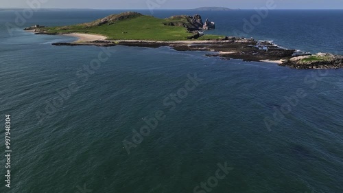 Ireland's Eye, County Dublin, Ireland, May 2023. Drone tilts up to reveal the picturesque Isle's beach and rugged landscape on a bright sunny day with Lambay Island on the horizon. photo