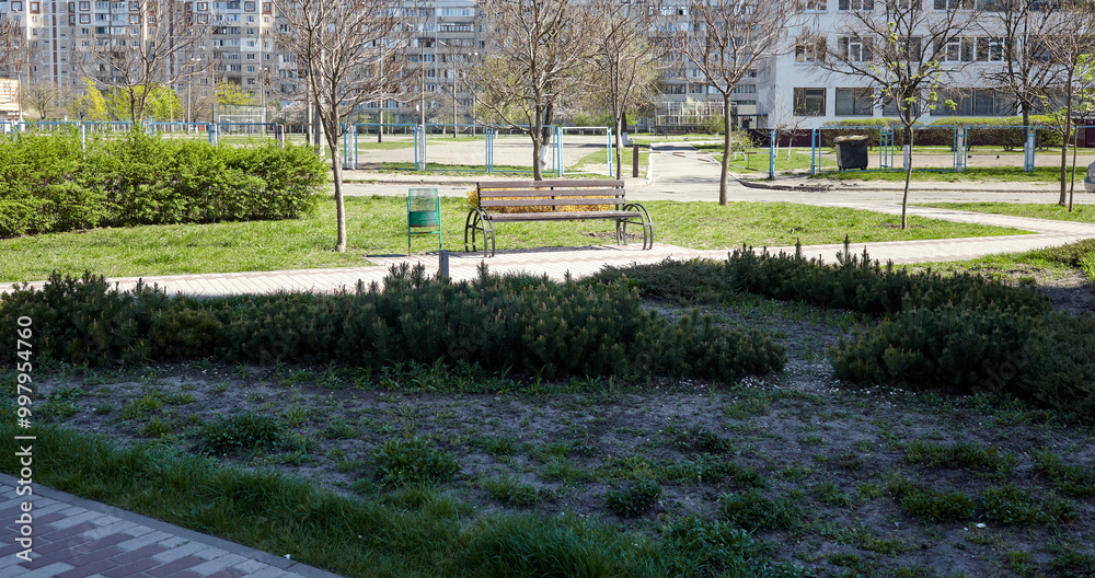 Obraz premium Rest area with bench surrounded by trees and ornamental shrubs in Kyiv, Europe. Place to rest in the city park at spring