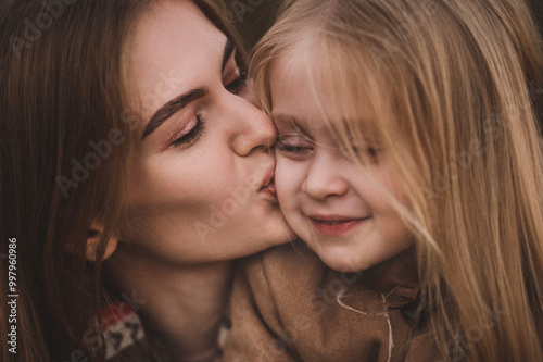 portraits of pregnant woman and her daughter walk through an autumn forest, along the beach near the river in stylish beige coats. Noise blurred toned vintage image