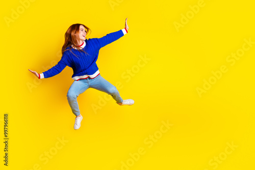 Photo of red hair jumping model young cheerful woman in blue stylish pullover and jeans white sneakers flying isolated on yellow color background