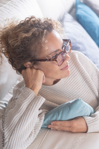 A serene adult woman in her 40s sitting comfortably on a cozy couch, smiling dreamily, embracing a balanced and healthy lifestyle. Peaceful, thoughtful, and content, she enjoys a tranquil moment photo