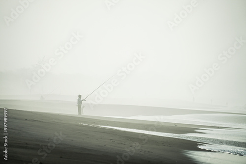 An Indonesian men silhouette is surf fishing in foggy beach at Pantai Congot, Kulon Progo. Surf fishing is land-based game fishing while standing on the shoreline. photo