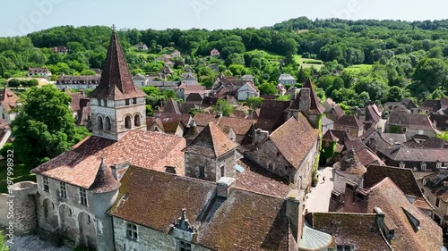 Aerial view of a beautiful village nestled along a peaceful river, with charming stone houses and a historic church surrounded by lush greenery.