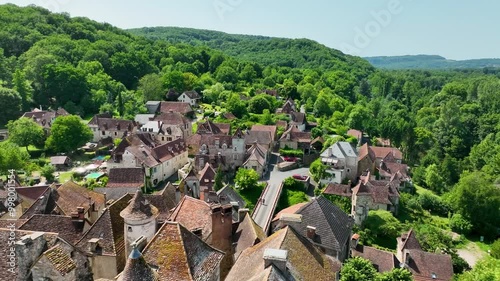 Aerial view of a beautiful village nestled along a peaceful river, with charming stone houses and a historic church surrounded by lush greenery.