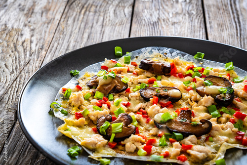 Vietnamese pizza - rice pepper omelet with mushrooms chicken meat and fresh vegetables served  on black plate on wooden table
 photo