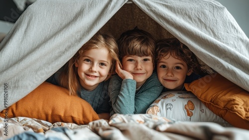 Three smiling children inside a cozy blanket fort, enjoying their playful moment.