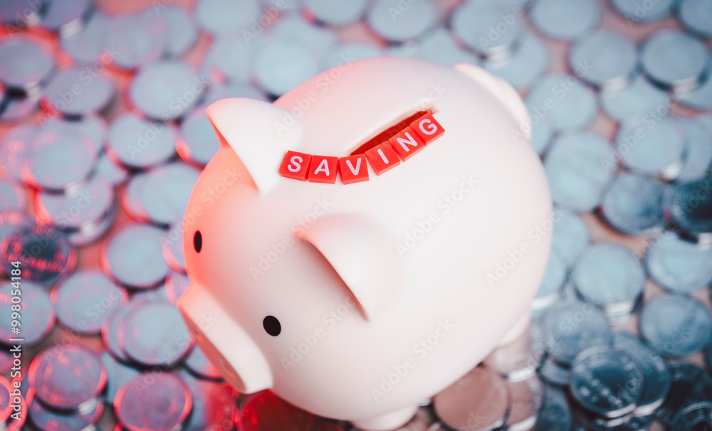 piggy bank surrounded by silver coins, with red letter tiles SAVING . saving money and financial security, personal finance, banking, and budgeting. financial growth and responsibility.
