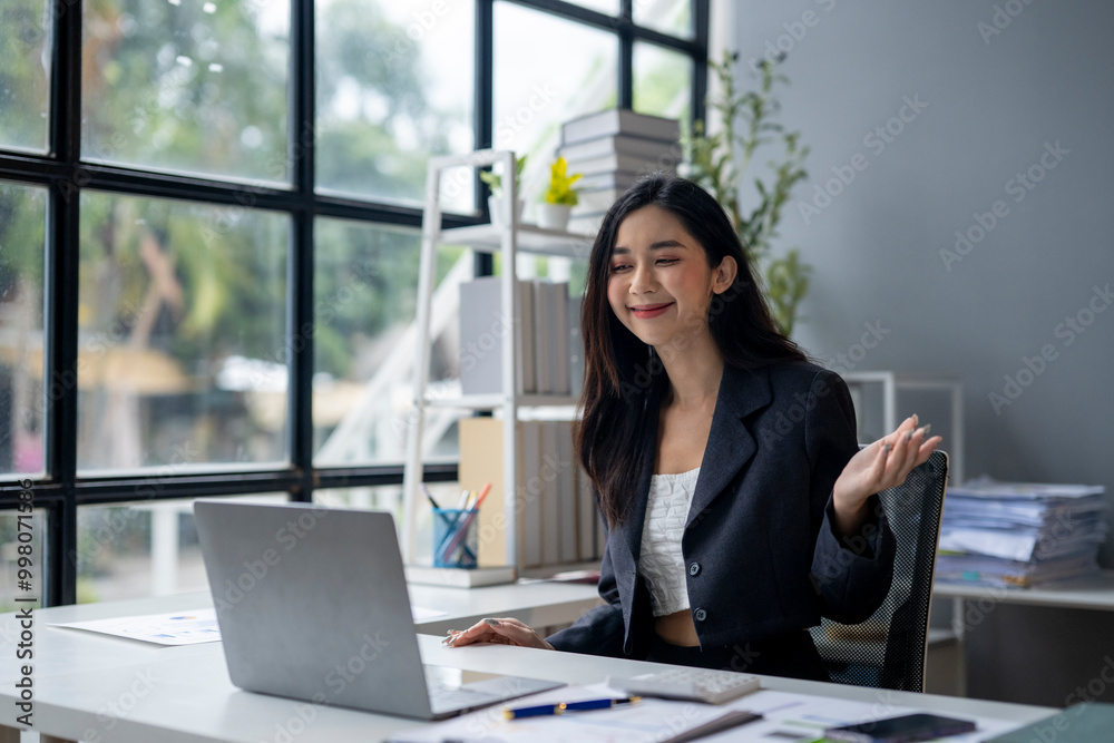 © apichat - A woman is sitting at a desk with a laptop in front of her