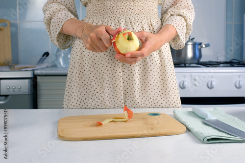 Woman peeling apple using knife cooking food dish on kitchen at home, hands close-up. Female housewife in dress preparing dish from apples. Culinary, cuisine, healthy eating, baking concept.