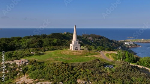 Killiney Hill, County Dublin, Ireland, June 2023. Drone swiftly orbits clockwise around The Obelisk with panoramic views of Killiney Bay and Dublin City Center in the distance on a bright sunny day. photo