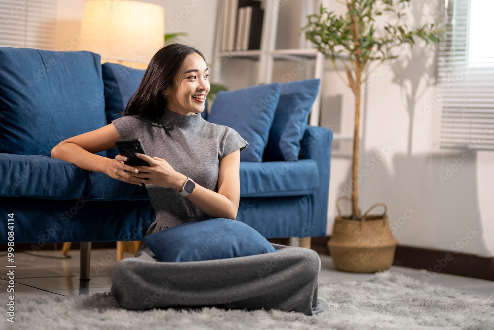 Young asian woman is using her smartphone while sitting on the floor in the living room Young asian woman is using her smartphone while sitting on the floor in the living room