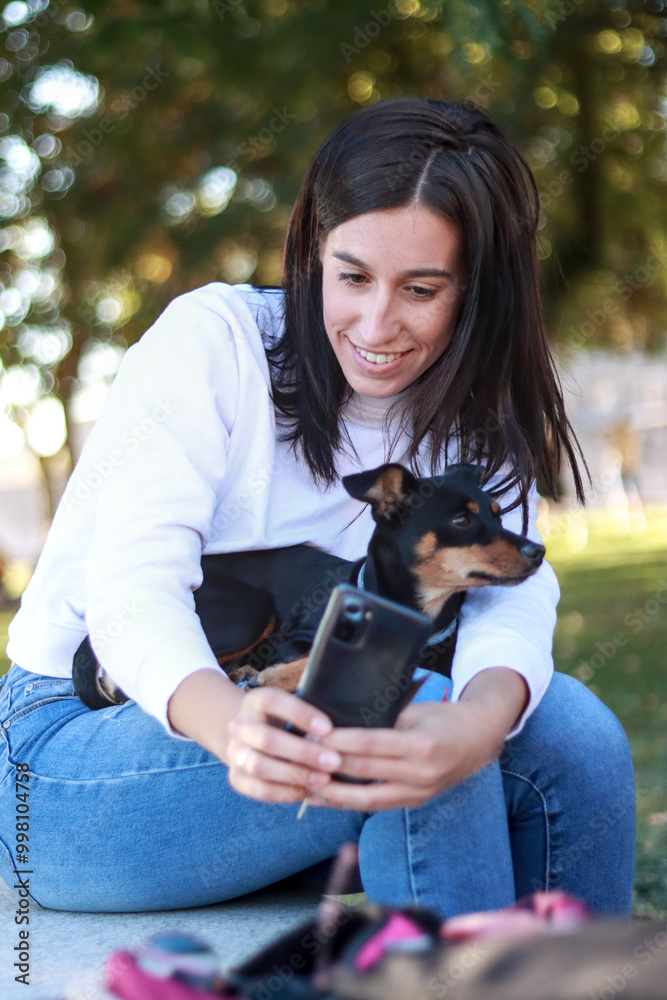 Young woman sitting outdoors in a park, taking a selfie with her ...
