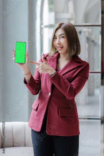 Businesswoman holding a smartphone with her right hand and pointing at the screen with her left hand.