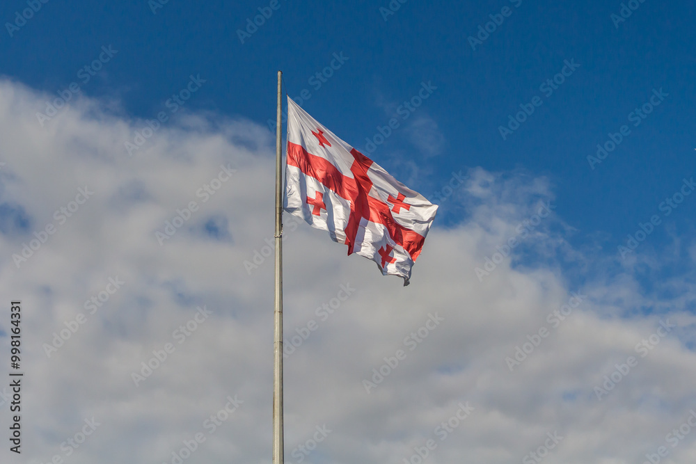 A large Georgian flag flutters against a cloudy sky. A large Georgian flag flutters against a cloudy sky.