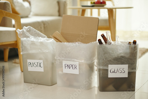 Three bins for recycling showing plastic, paper, and glass waste in living room environment showing dedication to environmental sustainability
