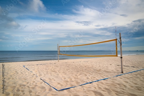 Sandy beach with yellow volleyball net, calm sea, and cloudy sky, tranquil setting