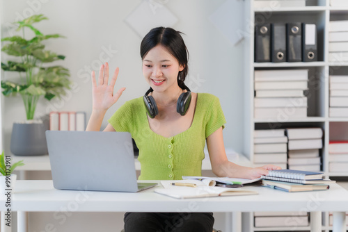 Virtual Connection: Young woman waves hello during a video call, showcasing modern remote work. 