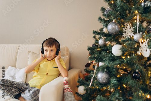 boy sitting on the sofa and listening to music on headphones, Christmas tree and anticipation of the holiday