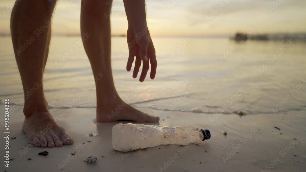 A person picking up a discarded plastic water bottle on a beach at sunset to cleanup coastal area, ocean in the background, concept of marine pollution A person picking up a discarded plastic water bottle on a beach at sunset to cleanup coastal area, ocean in the background, concept of marine pollution