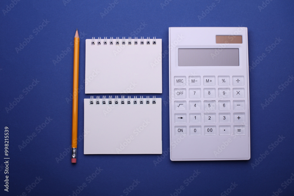 Group of Blank white spiral notebooks with calculator on blue background Group of Blank white spiral notebooks with calculator on blue background