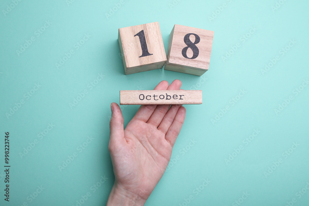 Hand holding wooden block calendar with date october 18 on mint green background Hand holding wooden block calendar with date october 18 on mint green background