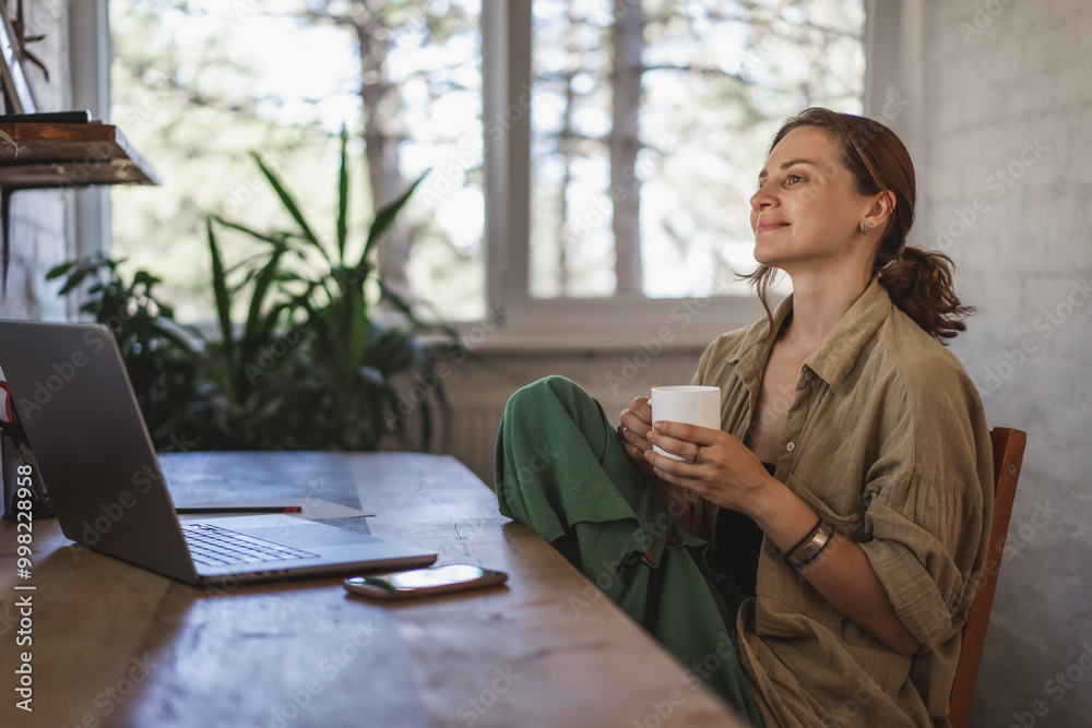 Dreamy happy woman student using laptop drinking coffee studying learning at home
