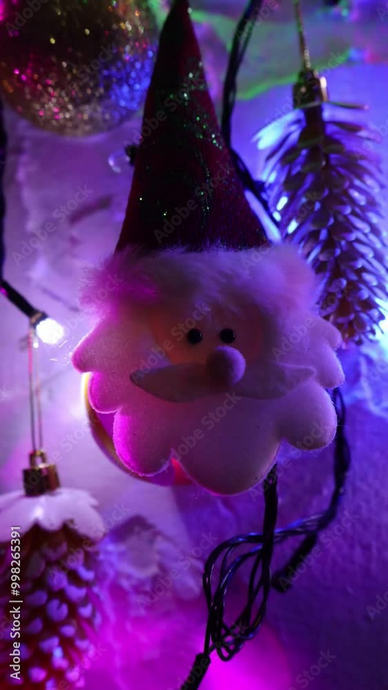 Una toma de cerca de una decoración de navidad y fin de año con una cara de santa claus  rodeado de varias luces con bombillos de varios colores en movimiento en la oscuridad. Video Vertical