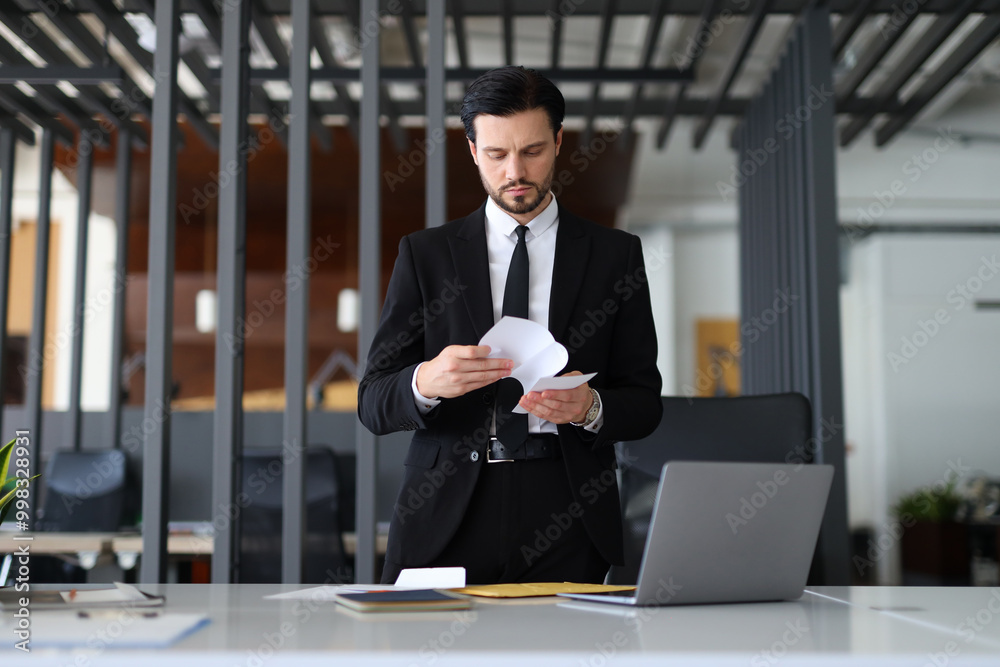 A man in a suit is reading a piece of paper at a desk. Concept of professionalism and focus, as the man is dressed in a suit and tie and he is reading important information A man in a suit is reading a piece of paper at a desk. Concept of professionalism and focus, as the man is dressed in a suit and tie and he is reading important information