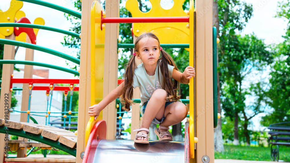happy preschooler girl playing on a slide on the playground in summer happy preschooler girl playing on a slide on the playground in summer