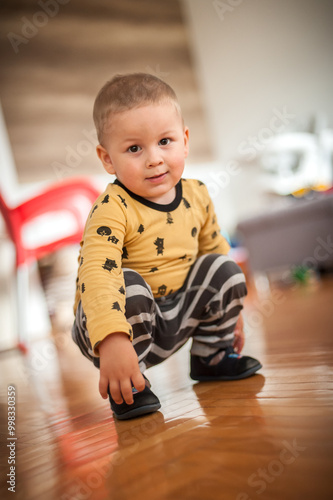 A playful toddler squatting on a polished wooden floor in a cozy indoor setting during the afternoon