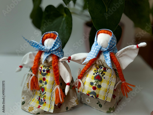 Two traditional Ukrainian motanka dolls with light blue headscarves and two long red braids each, standing side by side photo