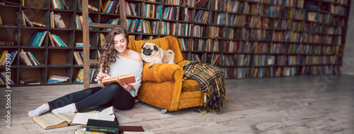 Εκτύπωση καμβά Smiling beautiful woman sitting on the floor in the library holding a book