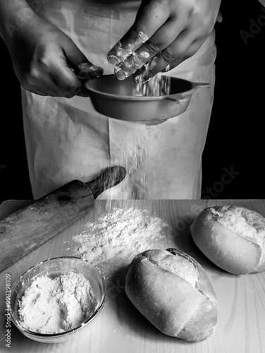 Hand sifting wheat flour on the table in bread preparation, and dark background. Black and white and vertical photo