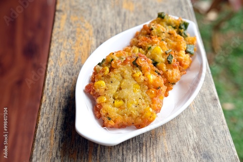 Crispy Indonesian corn fritters (Bakwan Jagung) served in a white dish.Made from sweet corn, flour, and herbs, fried to golden perfection.A popular traditional snack or side dish in Indonesian cuisine photo