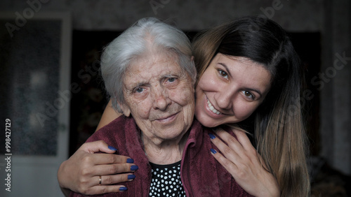 Smiling caucasian woman lovingly embraces and hugs her elderly old grandmother, meeting after being quarantined due to coronavirus pandemic. Close up portrait gaze look at camera. Caring for relatives