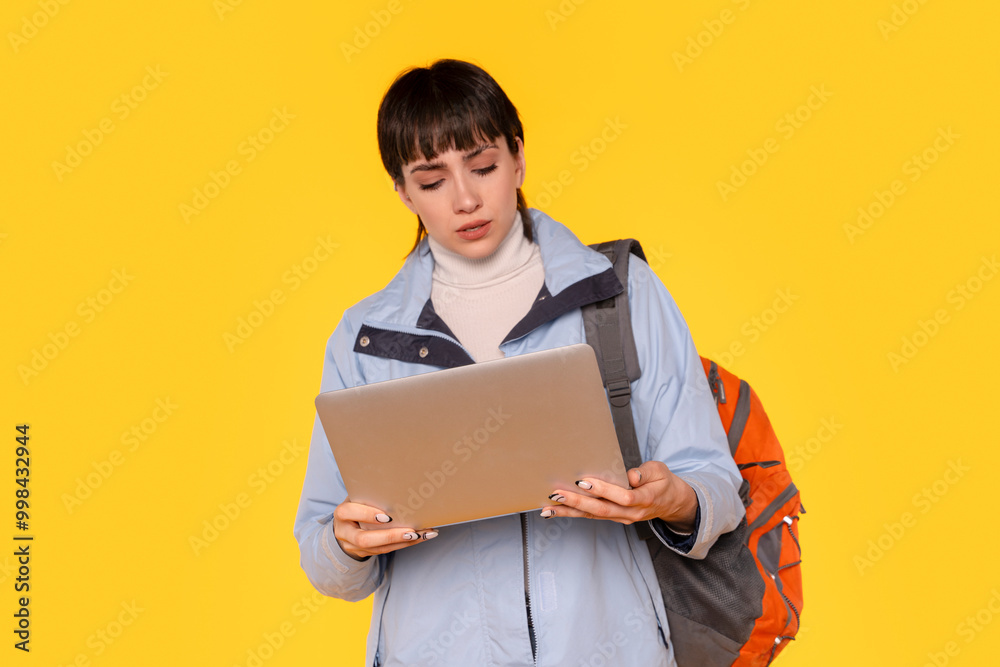 Young Woman in Blue Jacket Studies Her Laptop Against Bright Yellow Background Young Woman in Blue Jacket Studies Her Laptop Against Bright Yellow Background